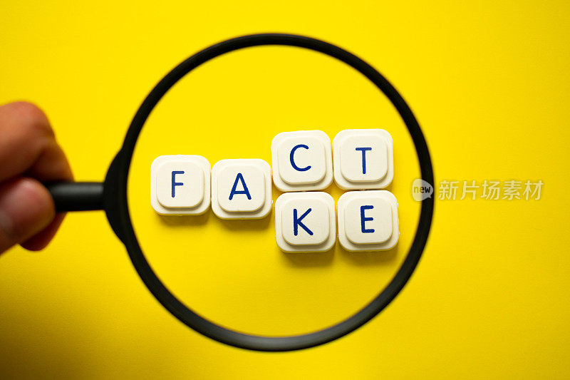 一个用放大镜看单词“事实/假”用字母游戏块在明亮的黄色背景上。区分事实与假新闻的概念。